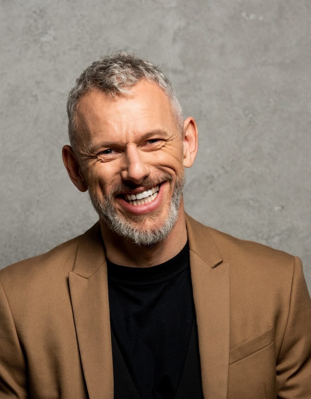 cheerful businessman in blazer looking at camera on grey